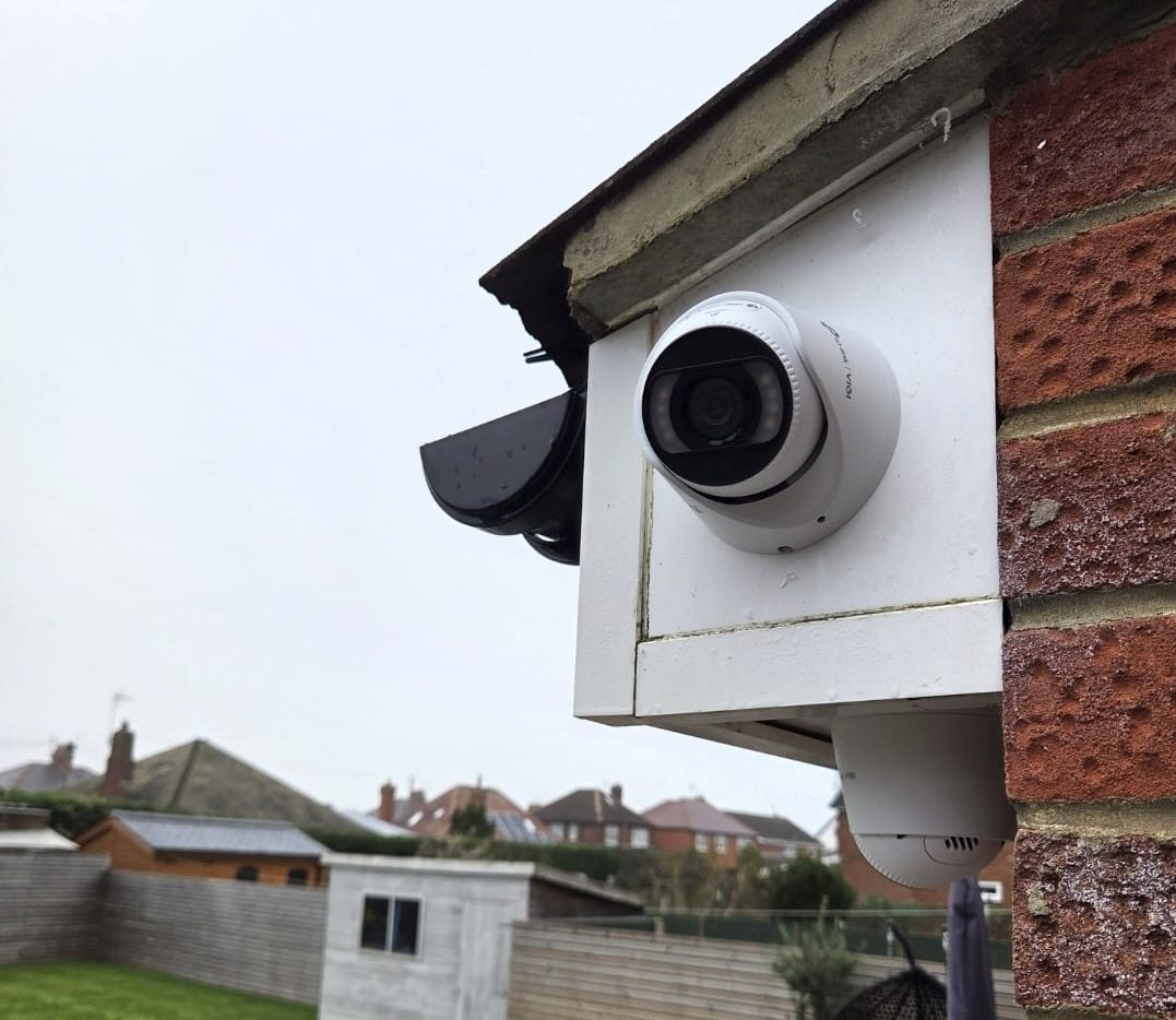 White Hikvision turret camera with weather hood under brick eaves